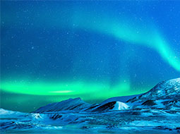 A breathtaking view of the Northern Lights illuminating a snowy landscape in the Arctic, with vibrant green and blue hues against a starry night sky.